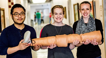 Three biomedical engineering students holding a model of a human leg they designed for the trainingof medical professionals.