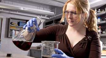 Female student examines dark liquid in a beaker.