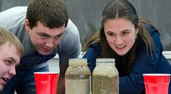 Two male students and one female student look at a soil sample.