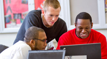 Three male students look at computer screen.