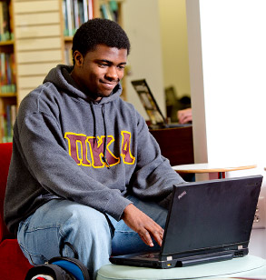Student sitting in the Moench Hall commons working on his laptop computer.