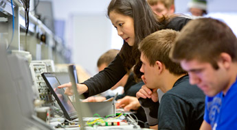 Female instructor points to laptop in electrical engineering lab.
