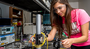 Female student manipulates device in physics laboratory.