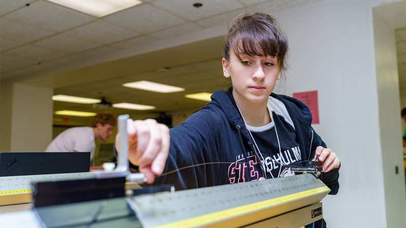 Female student uses scale in physics lab.