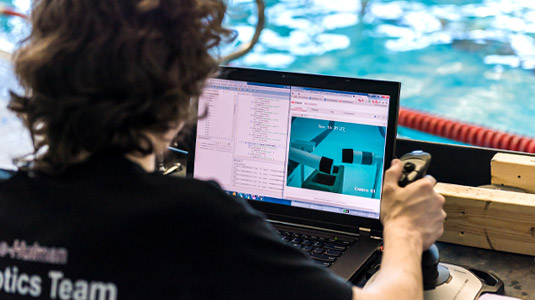 A student uses a joystick to drive an underwater robot, watching video from its camera on a laptop computer.