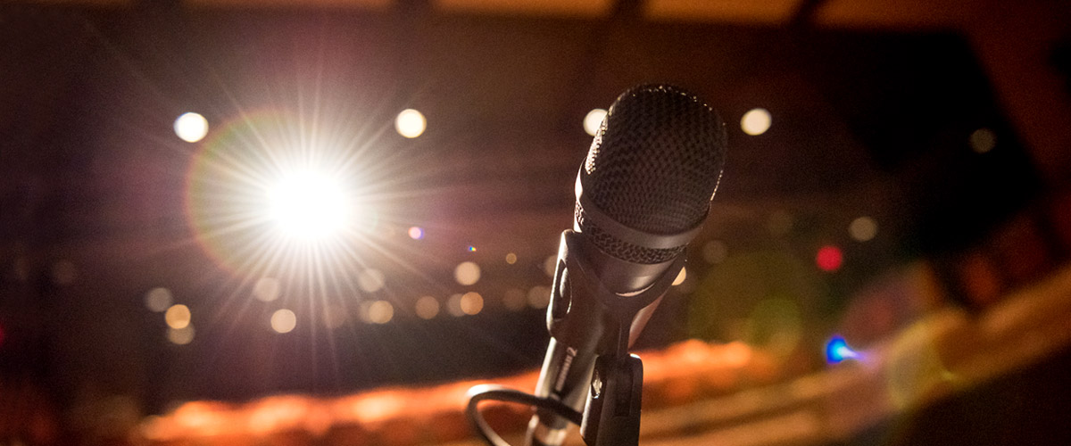 Close up image of microphone on a stand on the Hatfield Hall stage with a bright light and the auditorium in the background.