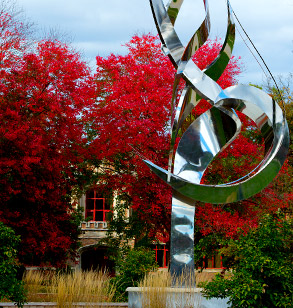 Flame of the Millennium sculpture on Rose-Hulman campus with fall foliage and Moench Hall in background.