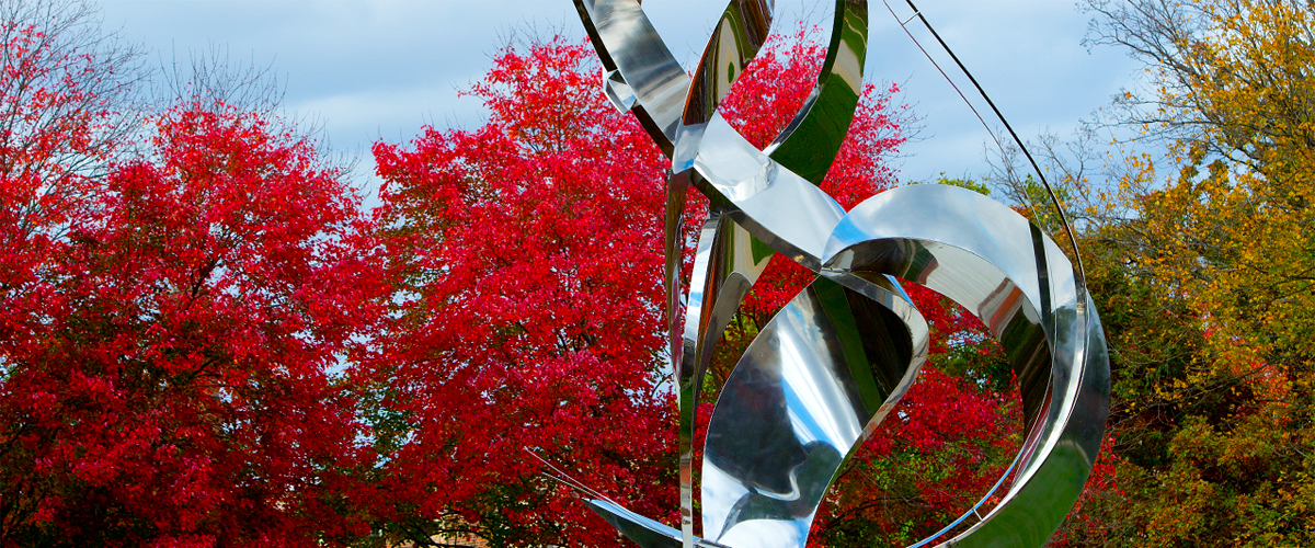 Close up view of the Flame of the Millennium sculpture with red fall trees in the background. 