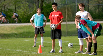 !Image shows four male soccer players standing on the intramural fields with the Heritage Trail bike trail in the background. Two bike riders are passing by on the trail.