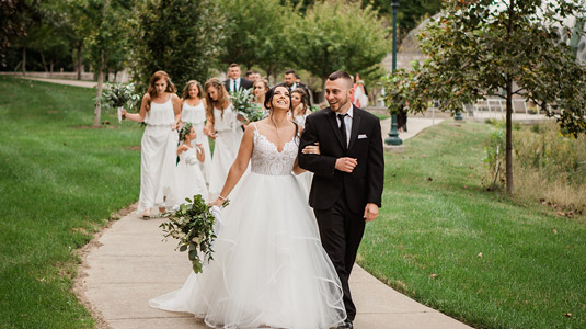 Smiling bride and groom walking with wedding party along the lake.