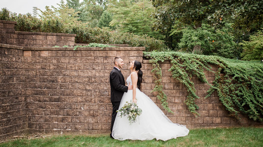 Bride and groom in front of retaining wall with greenery cascading over the side.