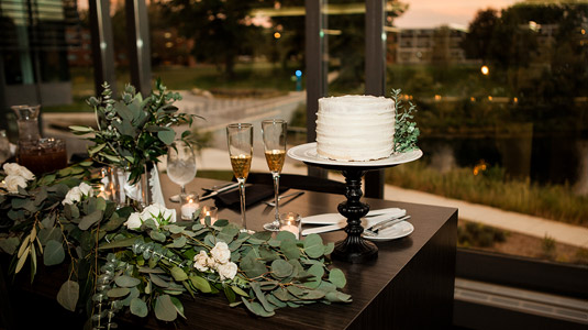Wedding cake and champagne glasses in front of widow at Vonderschmitt reception space.