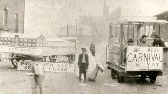 Historical photo showing a model of Moench Hall on a wagon, and sign reading “Big Rose carnival in May.”