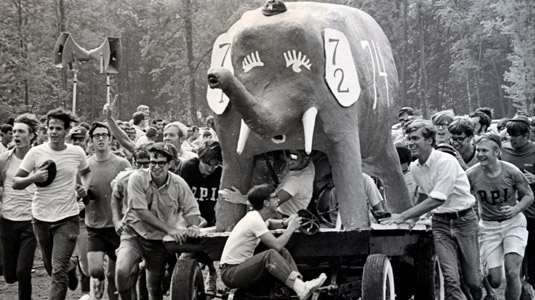 Students running and pushing a large papier mache elephant.