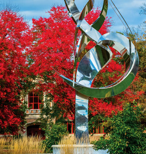 Flame of the Millennium sculpture in front of fall foliage.
