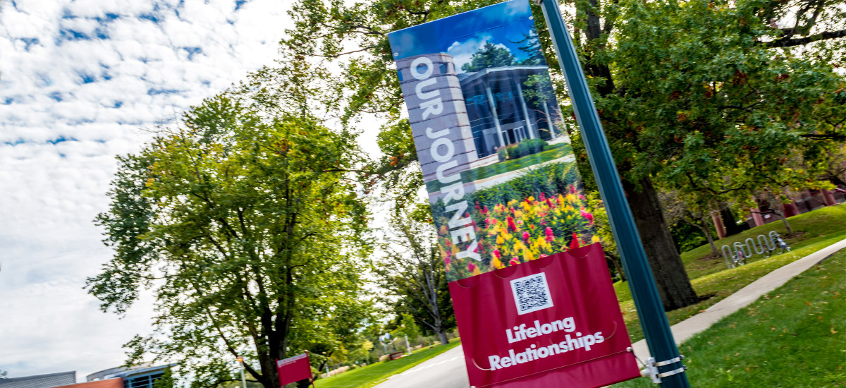 A banner featuring a picture of Hatfield Hall hanging on campus near green grass and trees.
