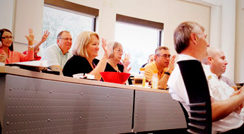 Faculty and staff smile and raise their hands participating in a RosePOD discussion session