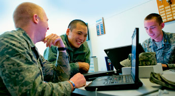 !Three male ROTC students smiling and working on laptop computers.