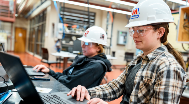 Female students wearing hardhat work in a lab.