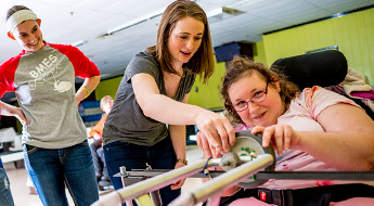 Students work with a woman using a specially designed device to enable disabled individuals to bowl. 