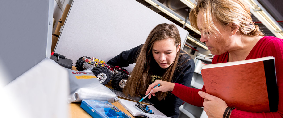 A female computer engineering professor shows a female student the correct way to proceed with a lab project. 