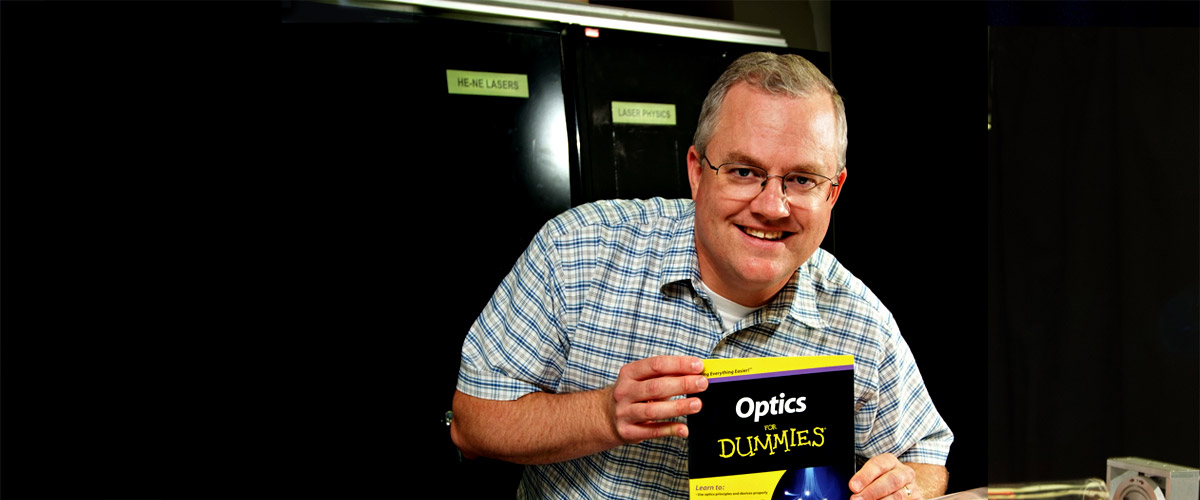 Professor Galen Duree holding a copy of his book, Optics for Dummies. 