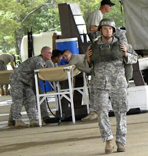 One man in uniform is walking, while a few other men in the background are leaning around a table