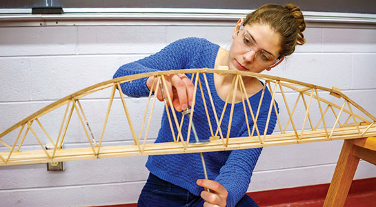 Female student testing engineering bridge project.