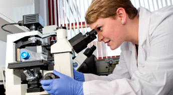 Student uses a microscope to conduct cancer research in a biology lab.