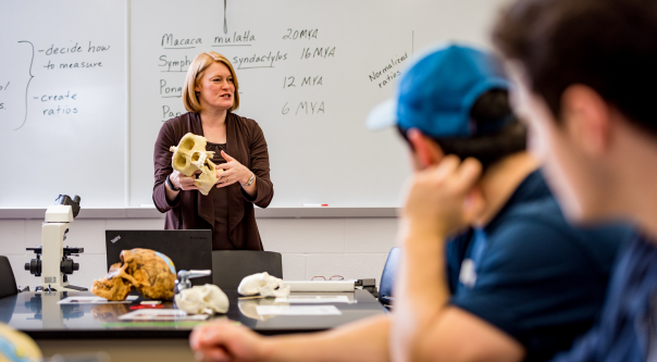 Several students and a professor watch as a student performs an experiment in a campus laboratory.  