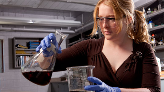 Female student prepares to pour liquid from beaker.