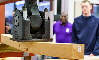 A student uses machinery in the structures lab to test the strength of a wooden beam.