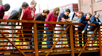Students stand on bridge and observe water below.