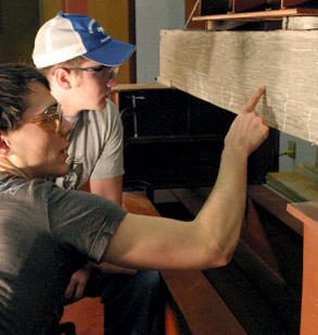 Two students observe long, wooden object in the lab.
