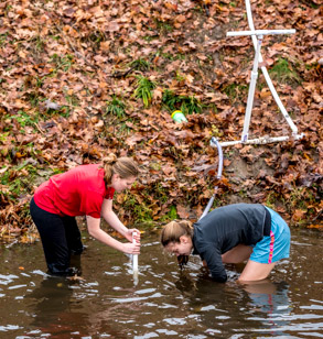 Two female students collect water samples from outdoor source.