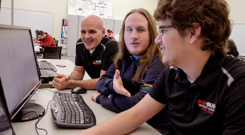 Students and faculty laughing and working together in a computer lab.