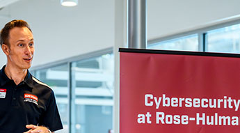 Image of faculty standing next to cybersecurity sign.