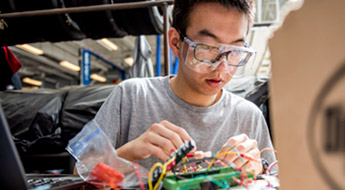 Male student works with wires and circuit board.