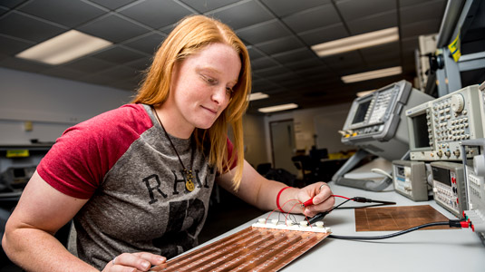 Male student holds robotic device as female professor takes notes.