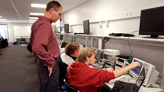 Male professor oversees students in computer lab.