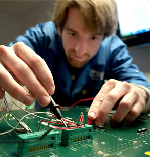 Male student uses a small screwdriver to assemble elements of a circuit board. 