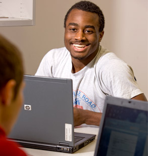 Smiling male student sits behind laptop.