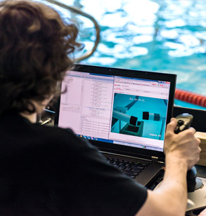 Student uses laptop and joystick to drive underwater robot in pool.