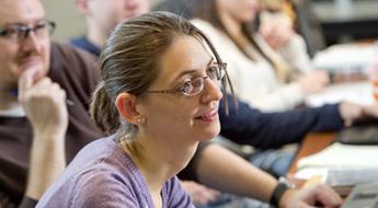 Three students smiling and watching a class presentation.