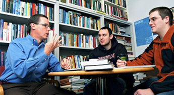 Economics Professor Kevin Christ meeting with two students in his office explaining an economics concept.