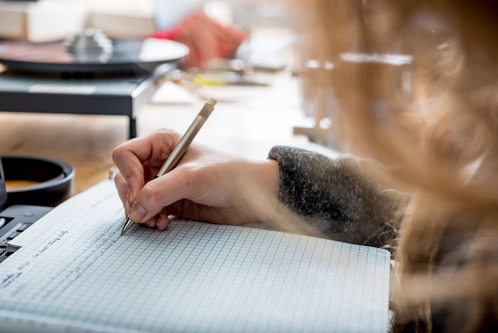 Student's hand holding a pen writing in a notebook. 