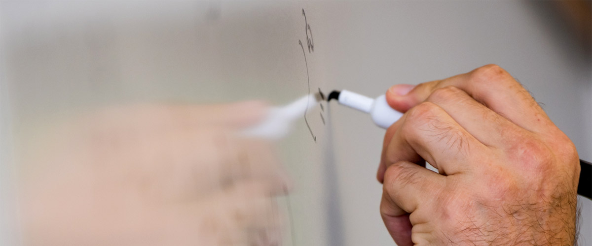 Teacher's hand holding a marker writing on a whiteboard. 