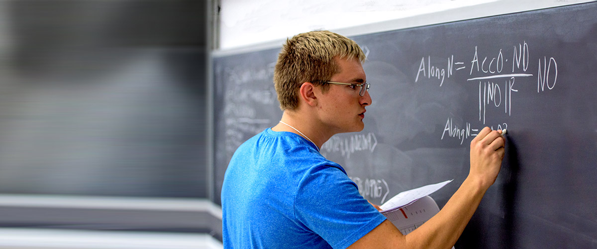Student solving a math problem on a blackboard.