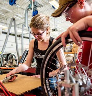 Female student cuts cardboard for a team project as male student assists in the Branam Innovation Center.