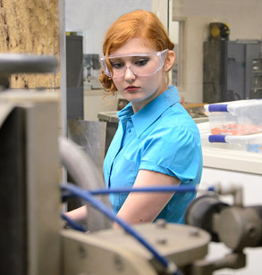 Female student wearing safety glasses looks at equipment.